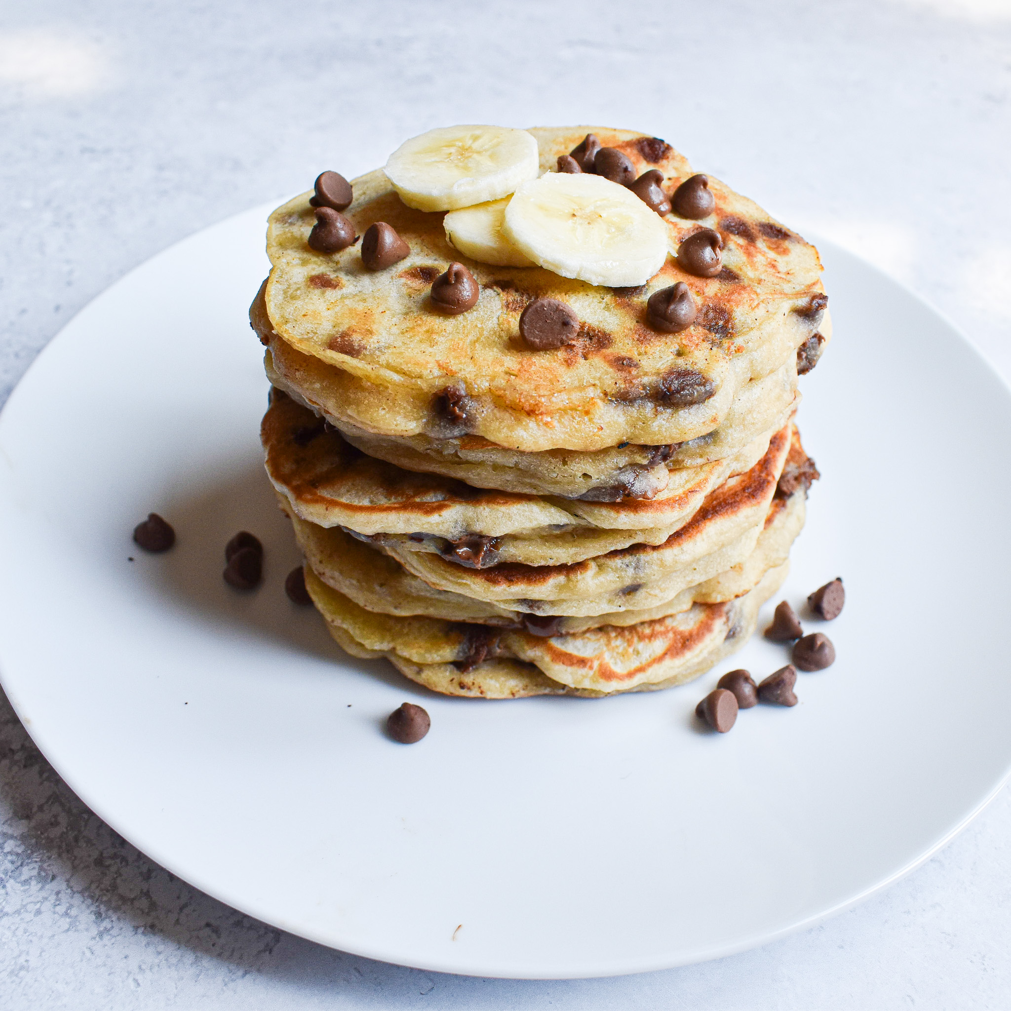 stacked banana chocolate pancakes on plate with chopped banana and chocolate chips on top for decoration. 