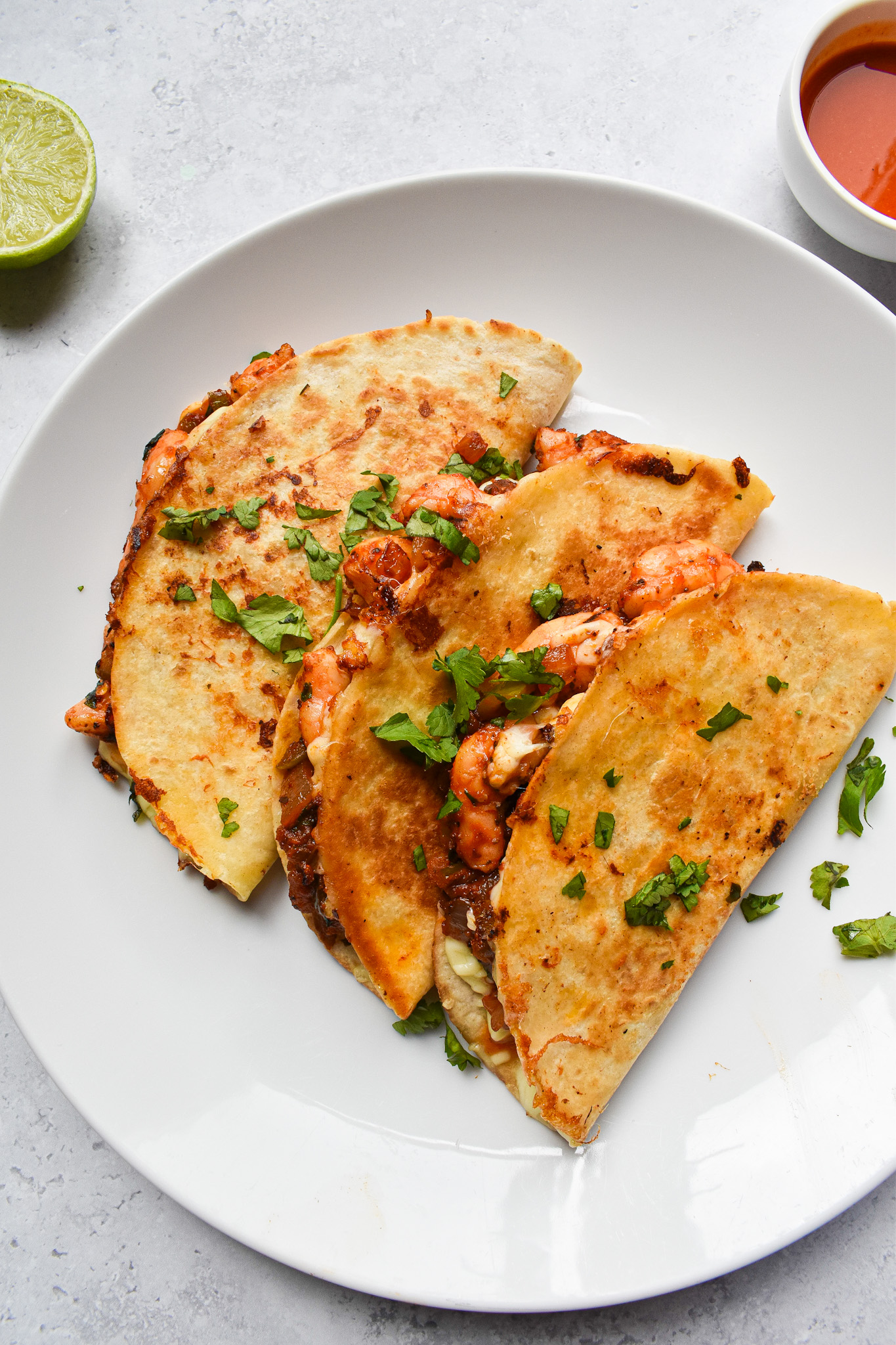 3 quesadillas on a white plate sprinkled with chopped coriander.