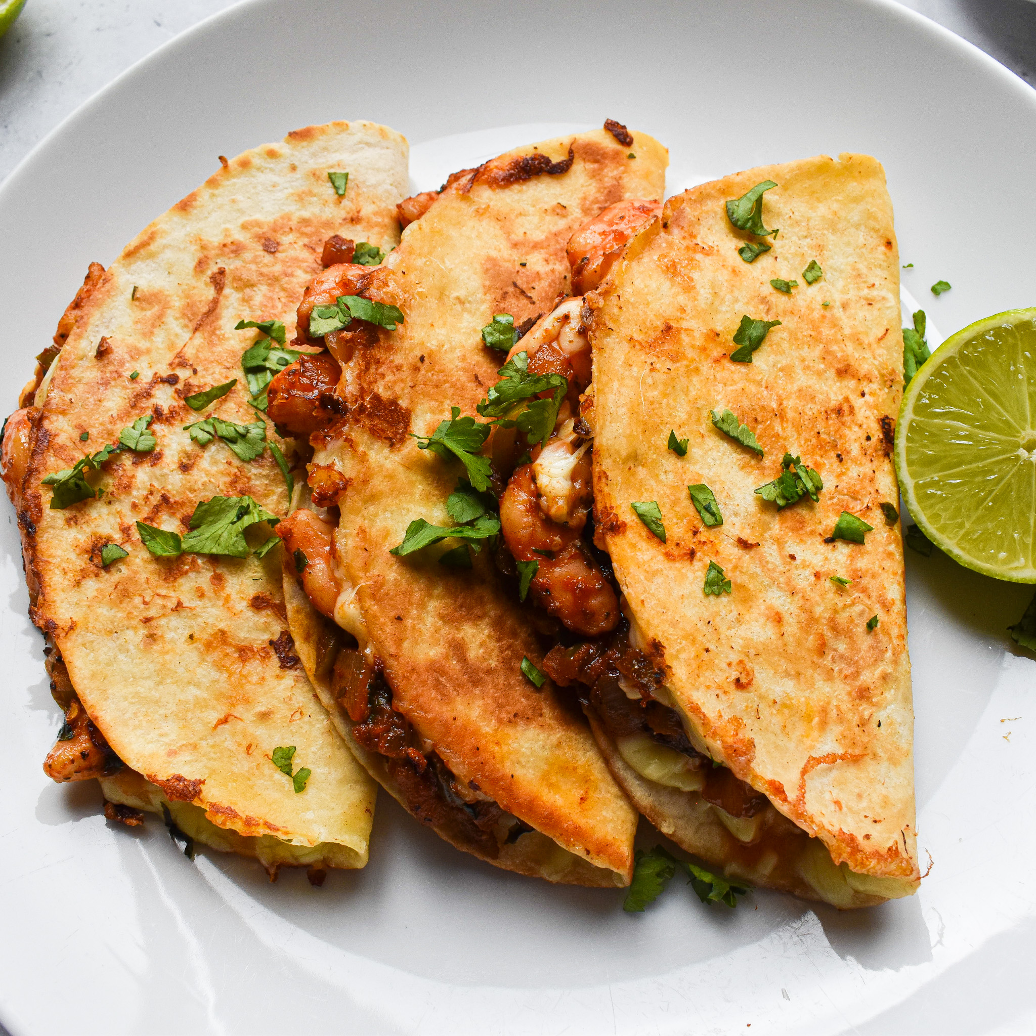 3 quesadilla tacos on a white plate with half a lime to the right.