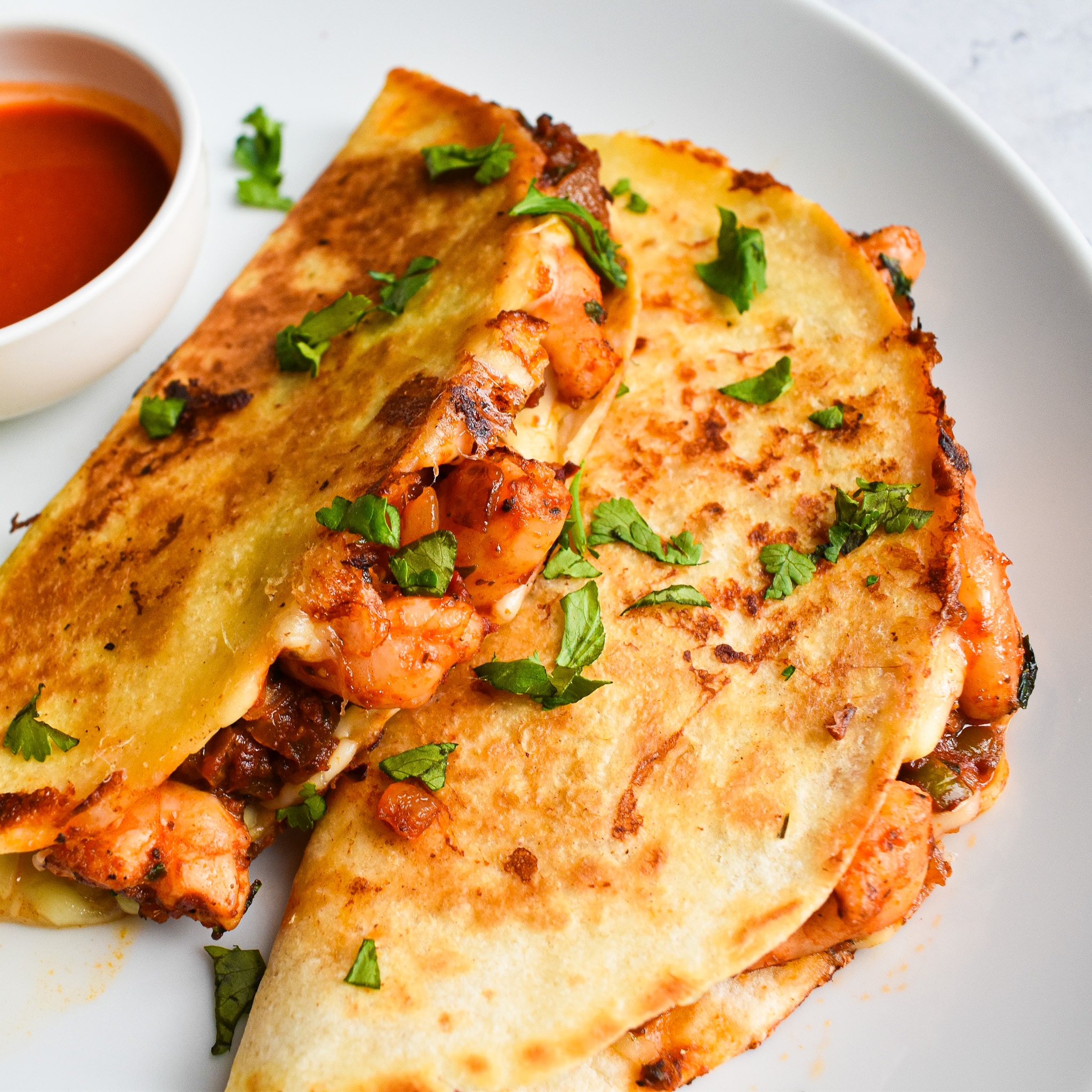 2 prawn tacos on plate with a sauce pot with hot sauce - chopped coriander sprinkled on for garnish.