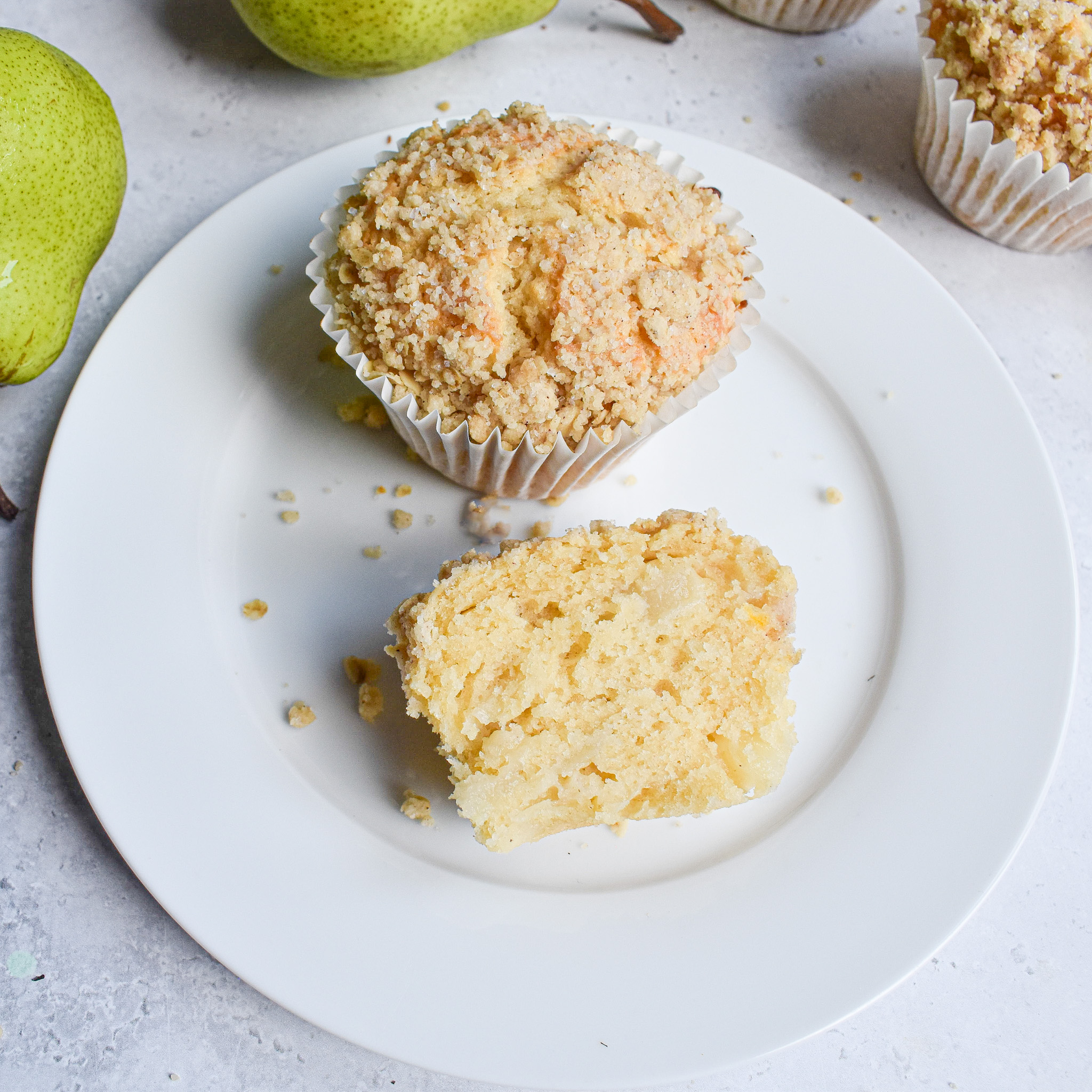 1 whole pear muffin on a white plate next to a muffin cut in half.