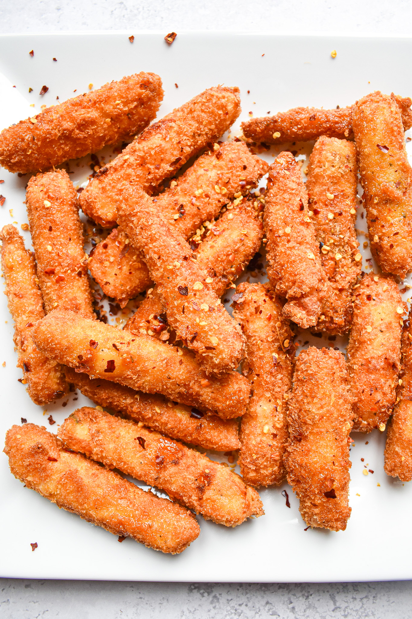 Hot honey halloumi fries on a white plate with chilli flakes sprinkled on top. 