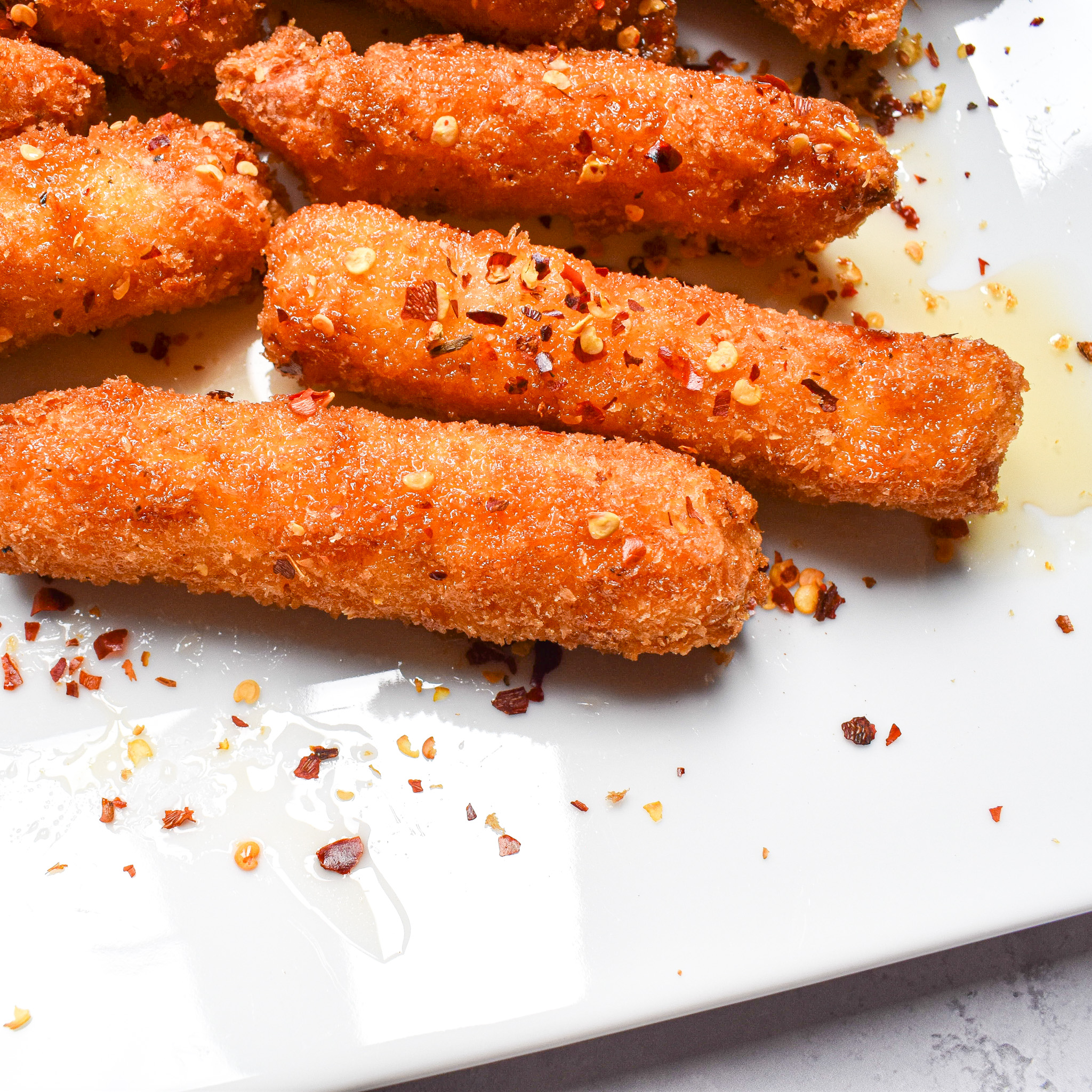 crispy cheesy sticks on a white plate with chilli flakes sprinkled on.