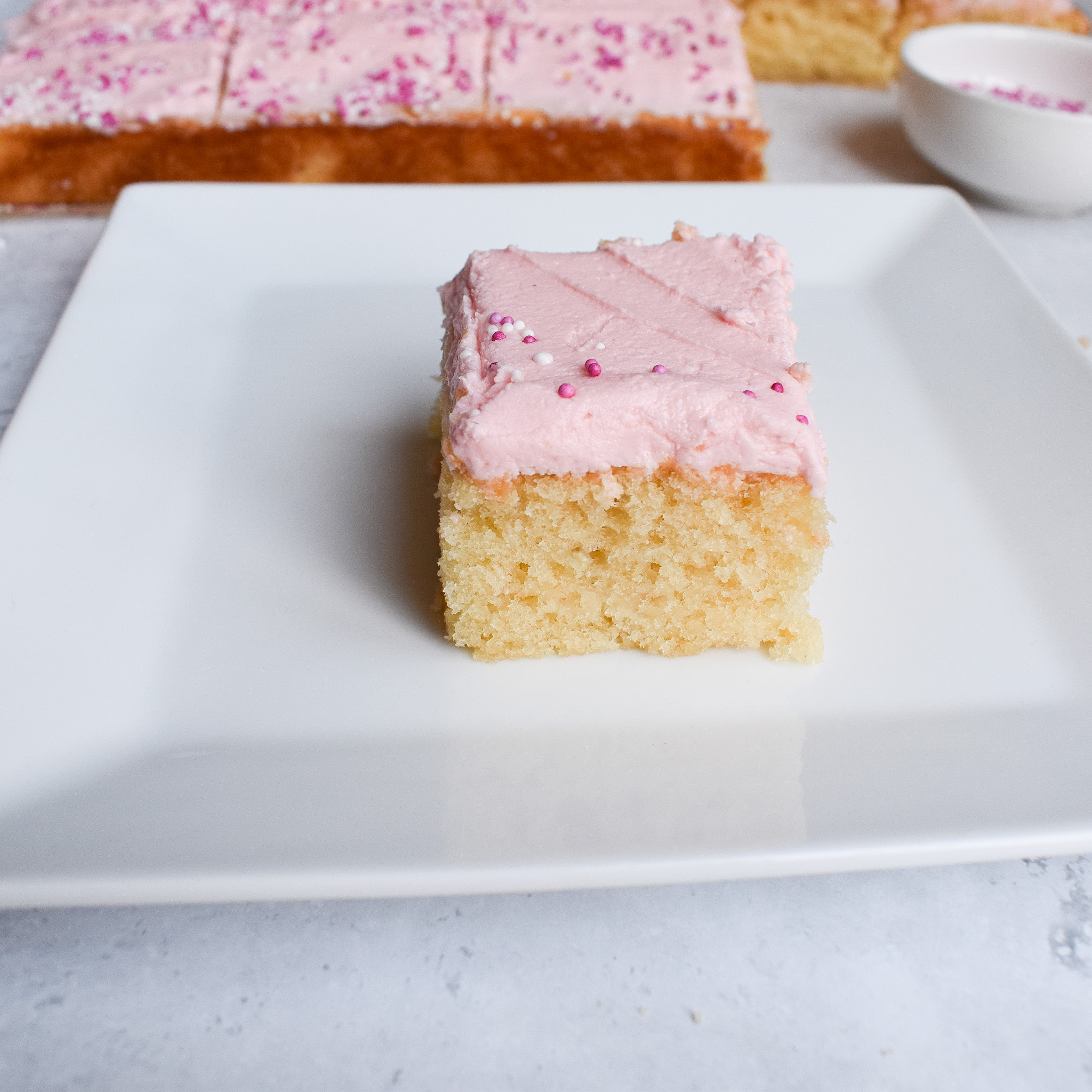 a piece of vanilla cake on a white plate with pink buttercream frosting.