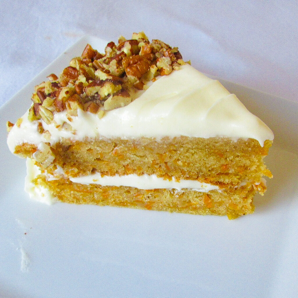 A slice of carrot cake with cream cheese frosting on a white plate.