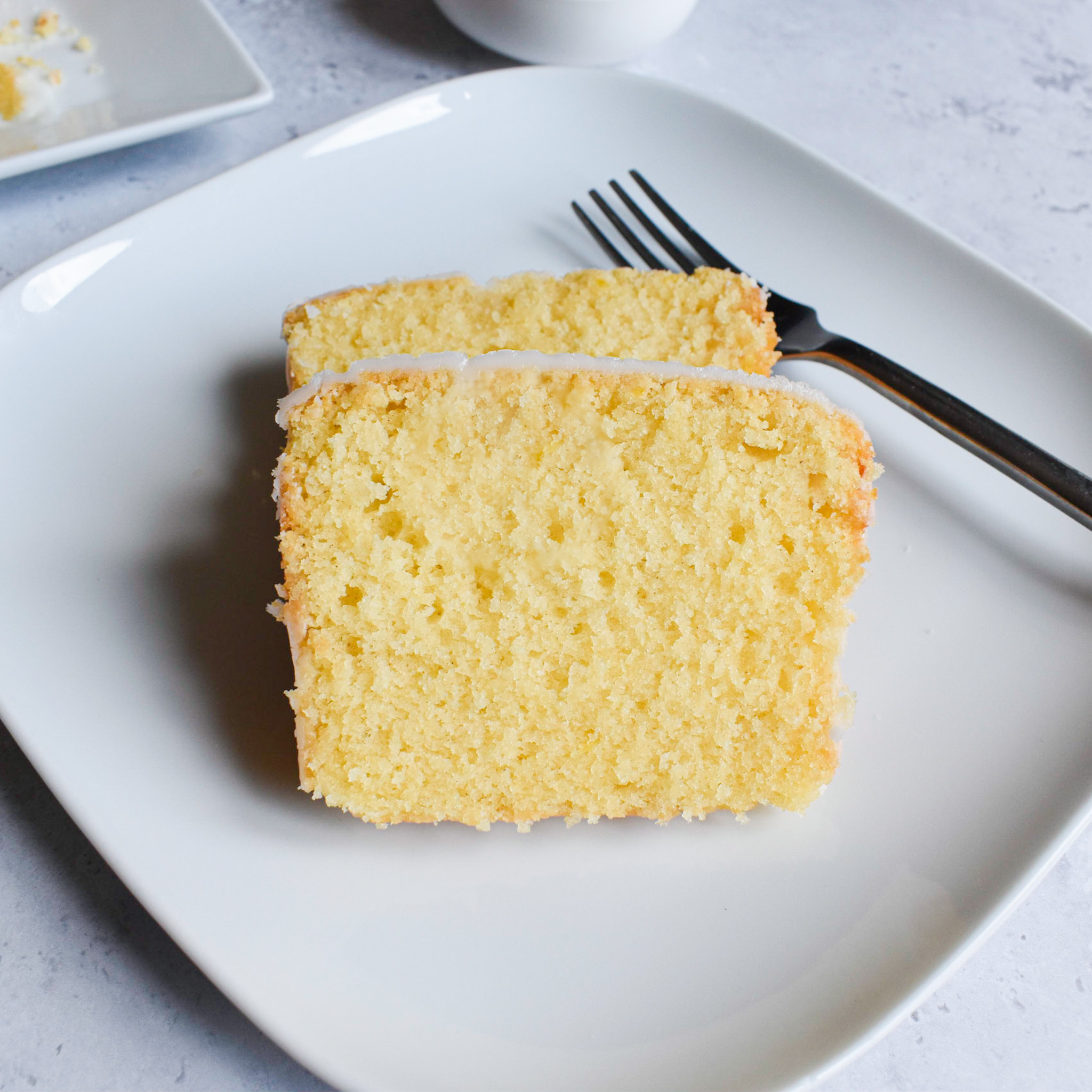 Lemon drizzle cake slices on white plate with a silver fork.